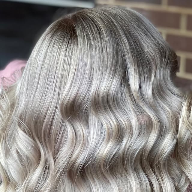 Silver-blonde waves with a soft grown-out root against a brick wall.
