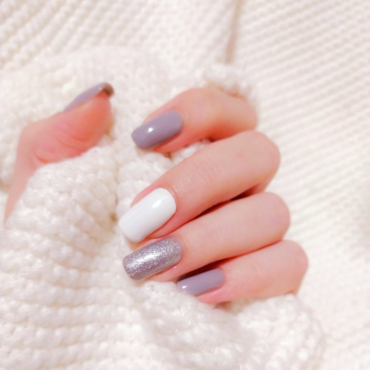 A hand resting on white knit fabric with a lilac and grey manicure and a silver glitter accent nail.