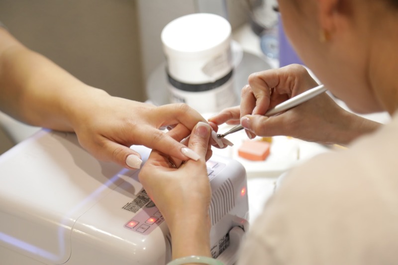 A nail technician shaping a client's nails at a manicure station.