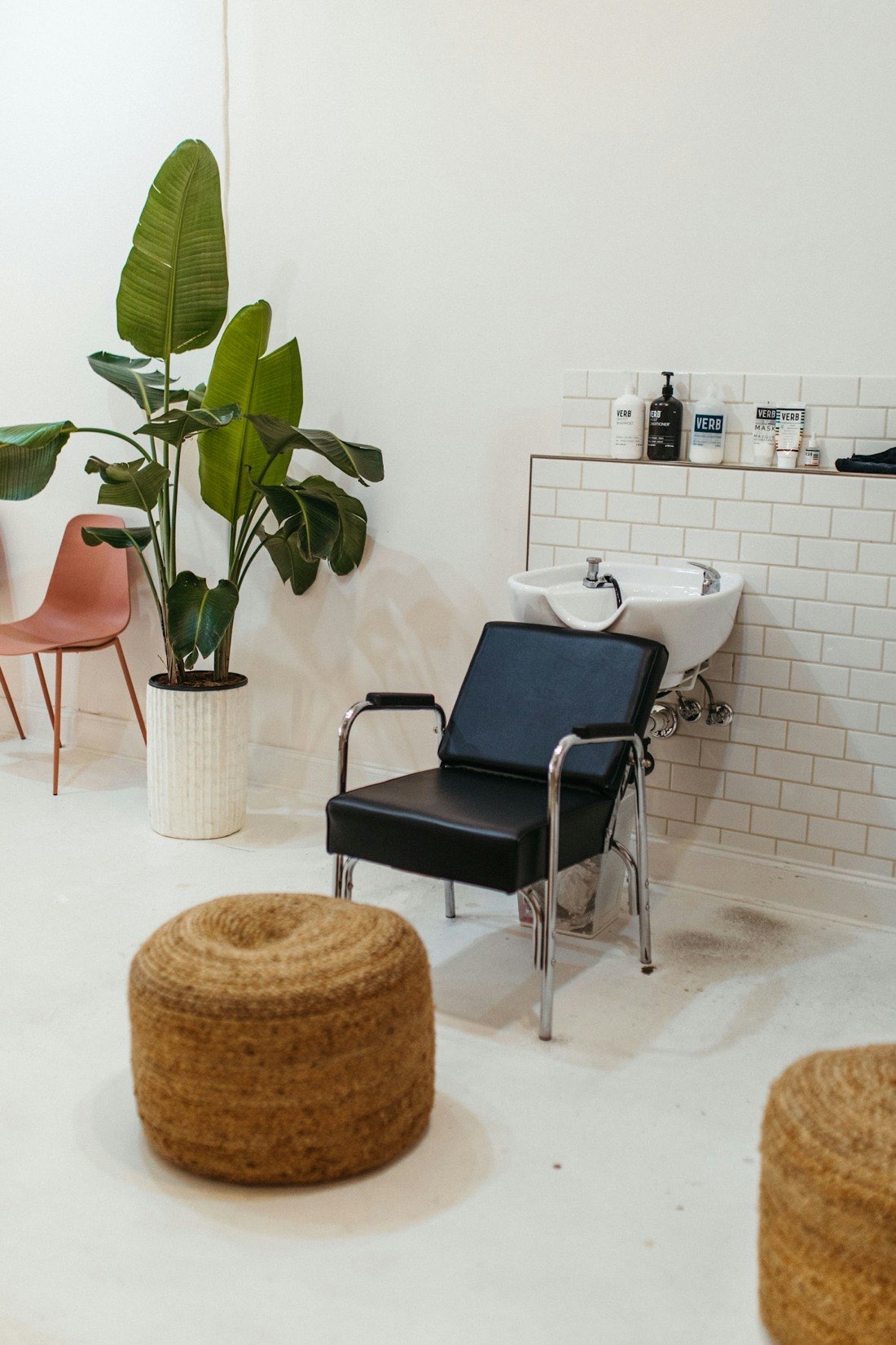 A bright salon washing station with a blush pink chair and a large potted plant.